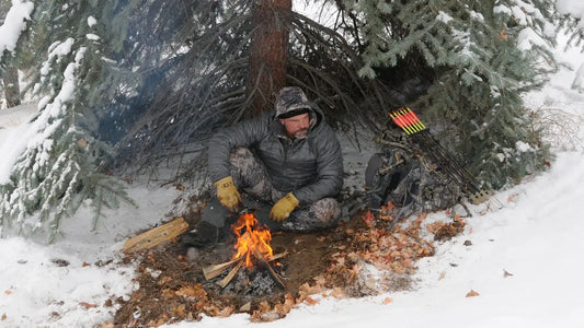Elk hunter by campfire under snowy pine, camo gear, modular hunting backpack & compound bow, winter archery hunt with best bow hunting backpacks