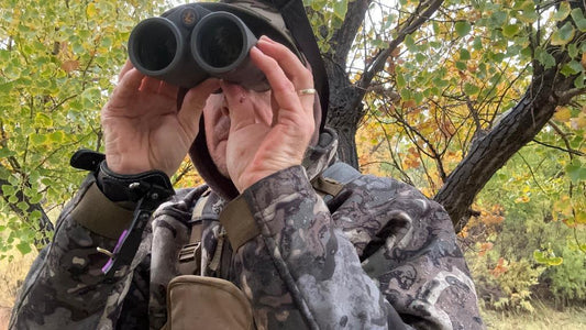 Hunter in camo uses binoculars for game observation in forest
