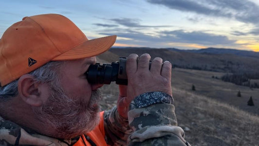 Hunter glassing for elk with binoculars on Wyoming hunting terrain at sunset