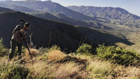 Hunter in camo trekking mountain hills with binoculars, treestand hunting gear scene with rolling desert mountain backdrop