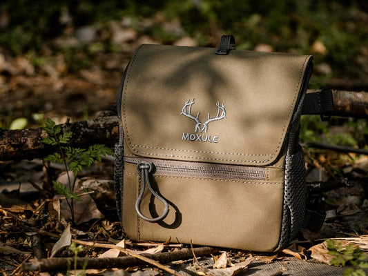 **Moxule camouflage rangefinder pouch with durable fabric and compact design rests on forest floor, ideal for hunting and outdoor gear accessories.**