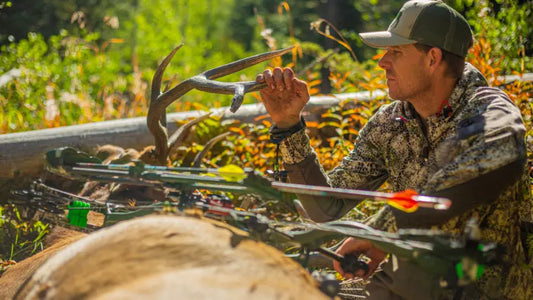 Camo‑clad elk hunter examines antler beside crossbow in wilderness