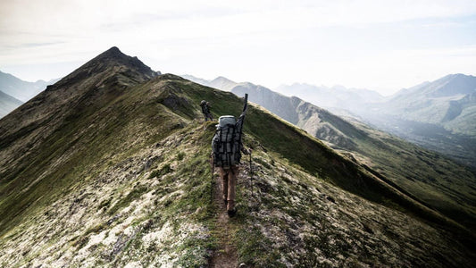 hunters with durable hunting backpacks trek a narrow alpine ridge, showcasing lightweight, comfortable backcountry hunting gear.