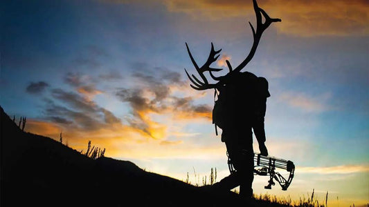 Elk hunter silhouette with trophy antlers on backpack at sunset