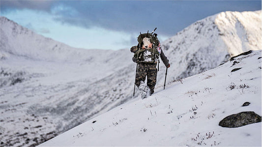 Hunter with heavy‑load multi‑day hunting pack hikes snow mountain backcountry during elk hunting season