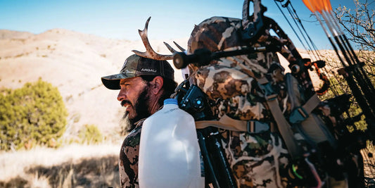 Hunter with loaded camouflage hunting pack carrying deer antlers in backcountry terrain