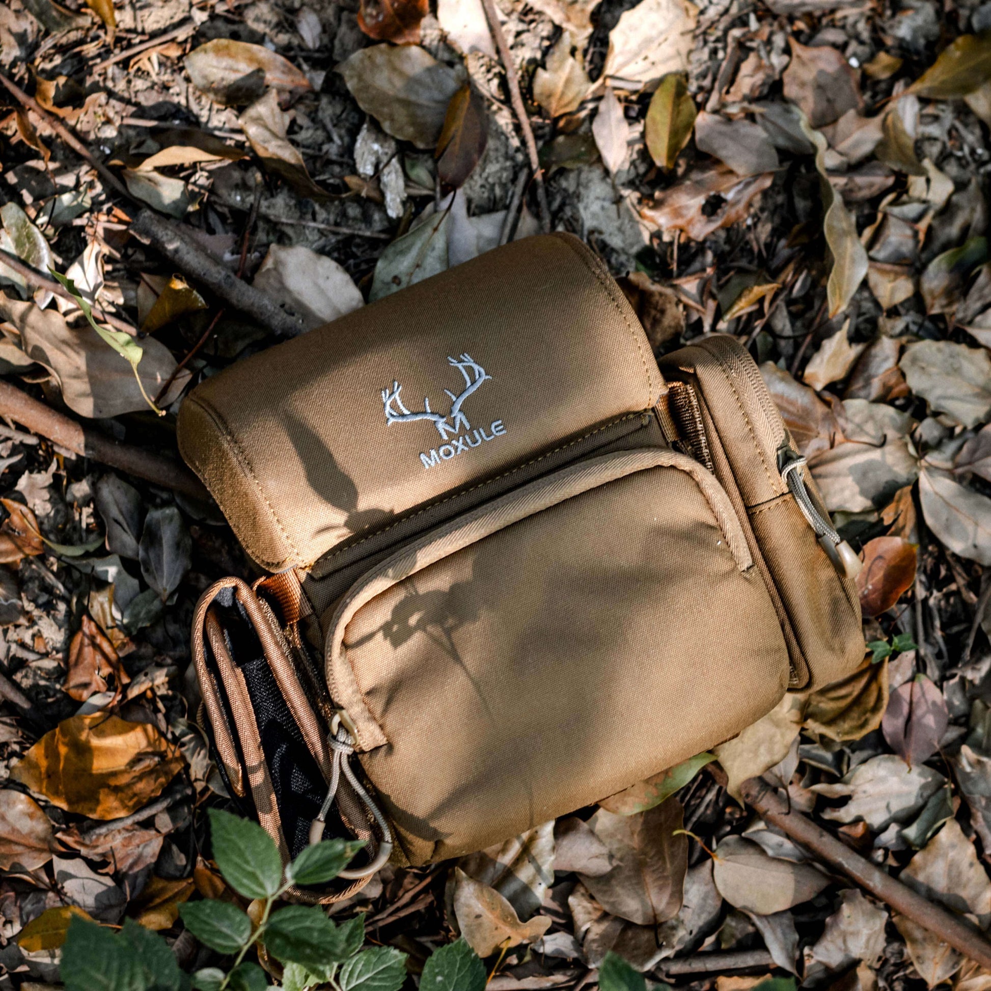 Moxule Tan Binocular Harness on Forest Floor | Rugged Hunting Gear
