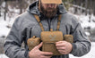 Hunter wearing Moxule coyote brown modular binocular chest harness in snowy woodland, adjusting bino pack, cold weather deer and elk hunting optics gear