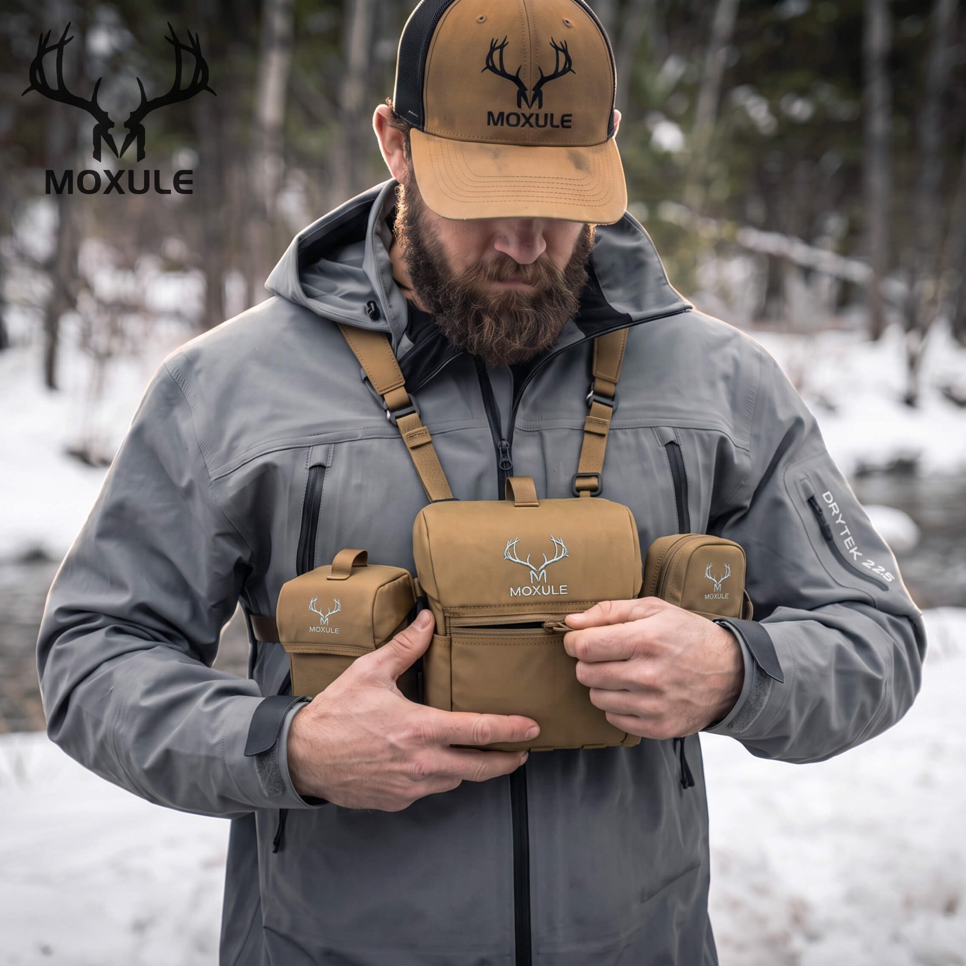 Hunter wearing Moxule coyote brown modular binocular chest harness in snowy woodland, adjusting bino pack, cold weather deer and elk hunting optics gear
