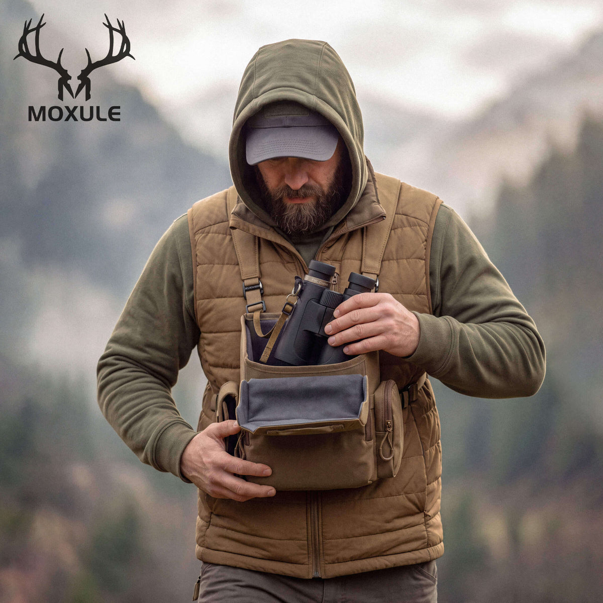 Hunter using Moxule R2 Pro binocular harness in mountain backcountry, tan chest pack holding binoculars for elk and deer hunting