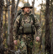 Hunter in camouflage walks through woodland wearing olive Moxule modular binocular harness, bino chest pack with detachable pouches for backcountry hunting