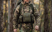Hunter in camouflage walks through woodland wearing olive Moxule modular binocular harness, bino chest pack with detachable pouches for backcountry hunting