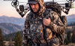 Bow hunter in camouflage outfit with Moxule bino harness and hunting pack, mountain backcountry hunting scene