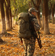Hunter in camouflage gear carrying Moxule PRO 3600 hunting backpack through autumn foliage. Equipped with rifle holder, water bladder compartment, and silent design