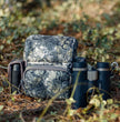 Modular camouflage binocular harness with accessory pockets, lightweight hunting chest pack for elk and deer hunting in the woods.