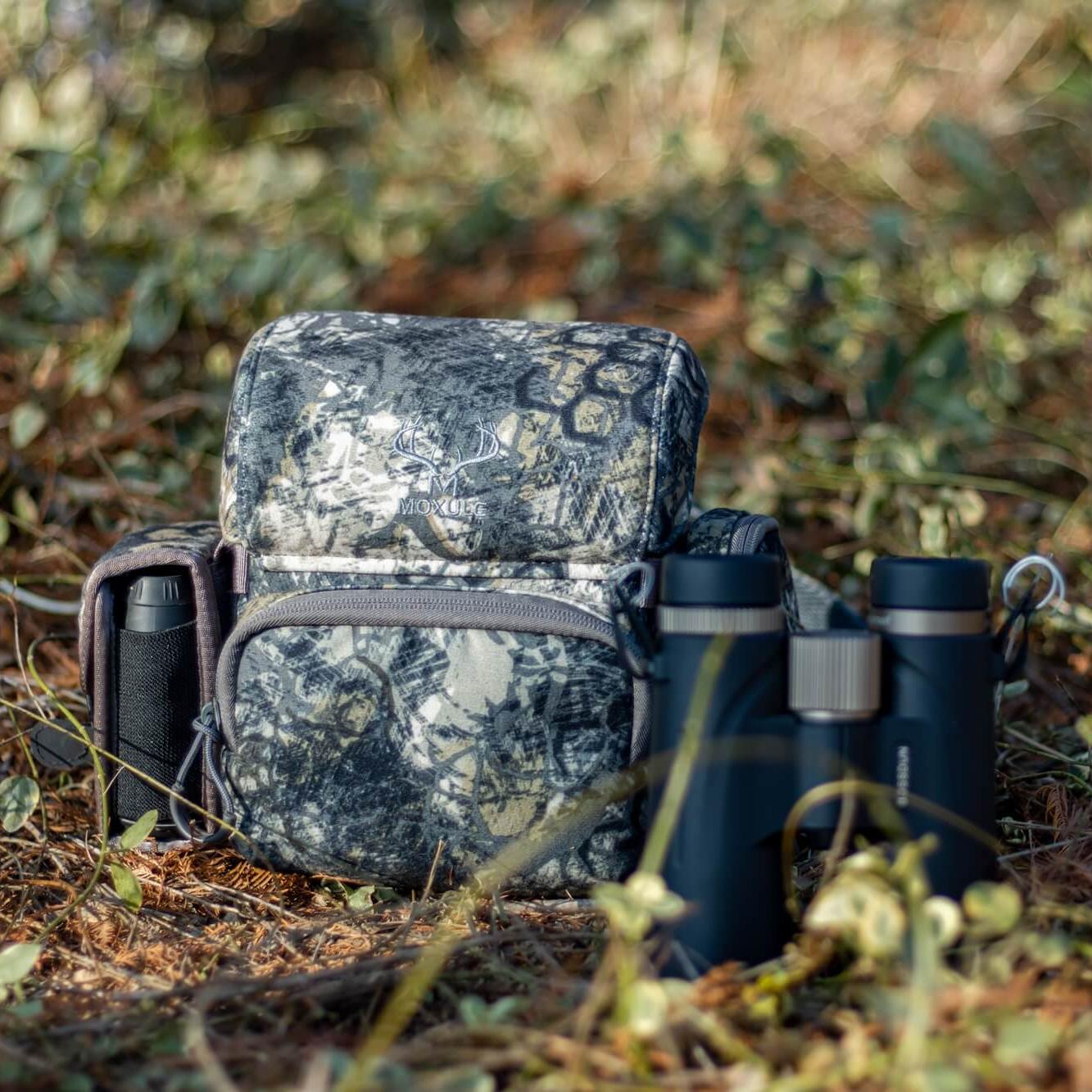 Modular camouflage binocular harness with accessory pockets, lightweight hunting chest pack for elk and deer hunting in the woods.