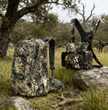 Camo hunting backpack with meat shelf and binocular chest harness combo, Moxule outdoor hunting gear for big game hunting in natural terrain.